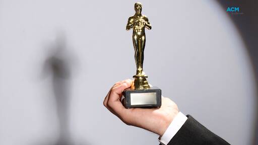 A hand from outside the frame holding an Oscar award. Picture via Canva. 