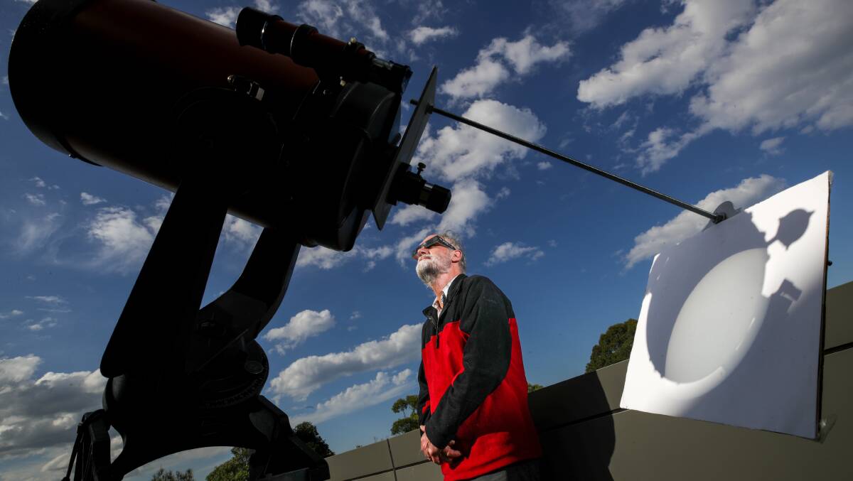 University of Wollongong Associate Professor Nicholas Jones wearing specialised solar eclipse glasses. He stands in between a telescope projecting the sun onto a board. Picture by Adam McLean