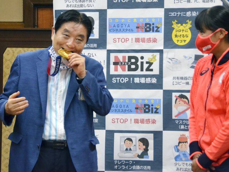 Nagoya mayor Takashi Kawamura biting the Olympic gold medal of softball player Miu Goto (right).